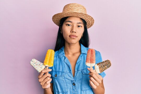 Young chinese woman wearing summer style holding ice cream relaxed with serious expression on face. simple and natural looking at the camera.