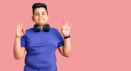 Little boy kid listening to music wearing headphones relax and smiling with eyes closed doing meditation gesture with fingers. yoga concept.