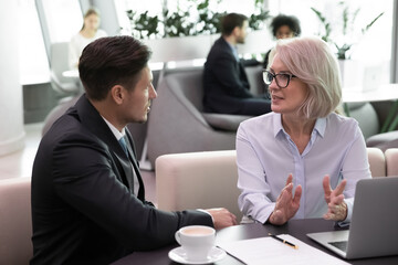 Diverse businesspeople sit at desk in office work on computer discuss cooperation or partnership....