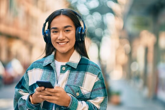 Young latin girl smiling happy using smartphone and headphones at the city.