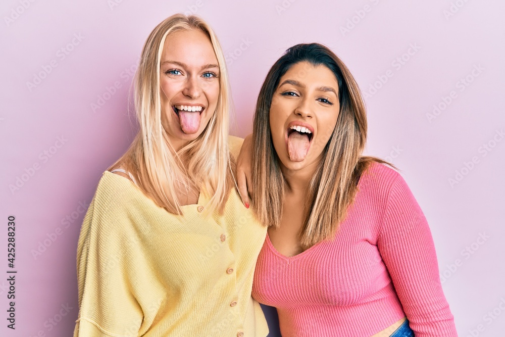 Sticker Two friends standing together over pink background sticking tongue out happy with funny expression. emotion concept.