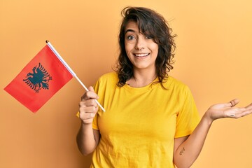 Young hispanic woman holding albania flag celebrating achievement with happy smile and winner expression with raised hand