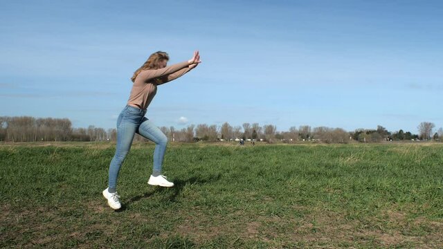 [4k] young blonde woman doing a cartwheel on a green field with blue sky in slow motion