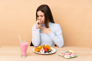 Teenager girl eating waffles isolated on beige background is suffering with cough and feeling bad
