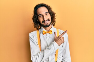 Young hispanic man wearing hipster elegant look cheerful with a smile of face pointing with hand and finger up to the side with happy and natural expression on face