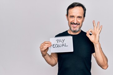 Middle age handsome man asking for social rights holding paper with pay equal message doing ok sign with fingers, smiling friendly gesturing excellent symbol