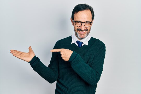 Middle age hispanic man wearing casual clothes and glasses amazed and smiling to the camera while presenting with hand and pointing with finger.