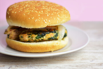 Homemade meat burger with vegetables, spinach. Served on a small white plate, wooden base and light pink background. Copy space.