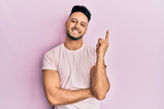Young arab man wearing casual clothes with a big smile on face, pointing with hand and finger to the side looking at the camera.