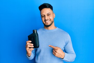 Young arab man holding motor oil bottle smiling happy pointing with hand and finger