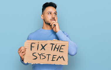Young arab man holding fix the system banner cardboard serious face thinking about question with...