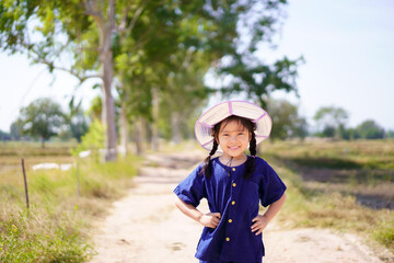 Asian child or kid girl gardener wearing mauhom shirt and hat with hands on waist and happy smiling in farm or garden for planting trees or forest and agriculture people on nature meadow and sun light