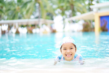 Fototapeta na wymiar Asian child cute or kid girl wearing swimsuit on swimming pool and smile broken tooth with happy fun in waterpark for learn swim or refreshing and exercise on vacation summer at hotel travel or school
