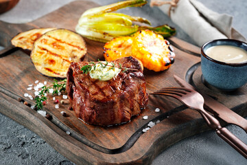 Grilled beef tenderloin steak served on a wooden board with butter and thyme. Filet Mignon recipe...