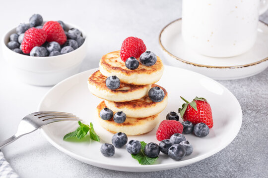 Cottage cheese pancakes with fresh berries, cup of coffee and on the table. Tasty breakfast food - Image