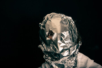 human head is wrapped with aluminium foil. only the right eye is looking throug a hole in the foil,...
