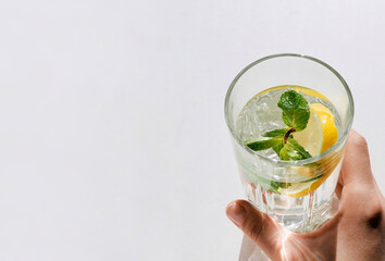 Woman's hand holding glass of water, lemon and mint. Wellness, healthy food, drinks, diet, detox. Summer drink Lemonade