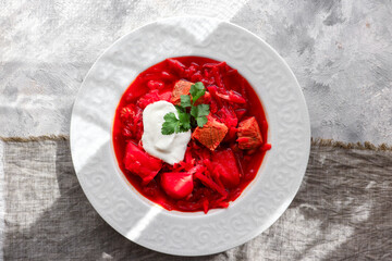 Red borsch with vegetables and meat in a white plate. Tomato soup. Light background. Delicious healthy lunch. Top view