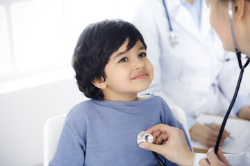 Doctor-woman examining a child patient by stethoscope. Cute arab boy at physician appointment. Medicine concept