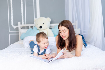 Obraz na płótnie Canvas mom reads a book to the child or teaches him at home on the bed Happy loving family. Mom and son