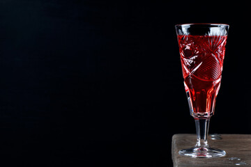 Berry liquor in crystal vintage shot glass on the wooden table against the black background