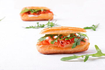 Eclair with salted trout, cream cheese and arugula on the white table