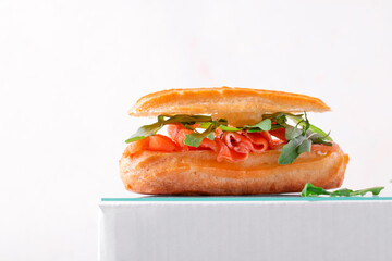 Eclair with salted trout, cream cheese and arugula on the white podium. Savory appetizer