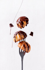 Covering profiteroles with chocolate glazing on the fork against the white background. Levitating food. French choux pastry dessert