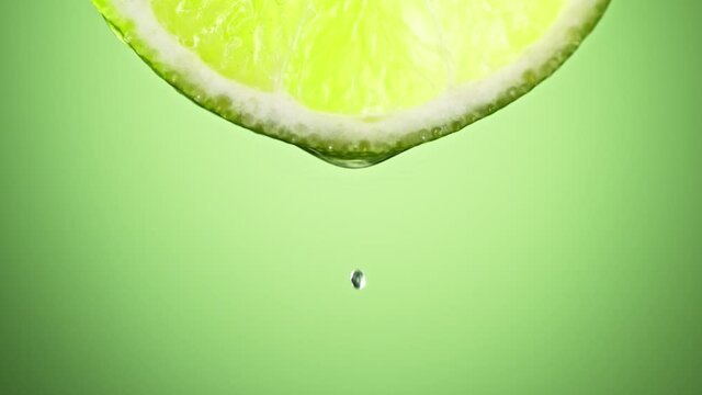 Super Slow Motion Macro Shot of Lime Juice Drop Falling from Lime Slice on Green Background at 1000fps.