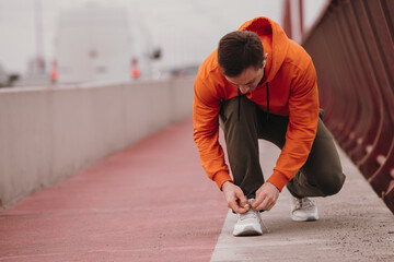 Athlete runner man tie shoelaces on his sneakers on a bridge