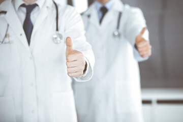 Group of modern doctors standing as a team with thumbs up or Ok sign in hospital office, close-up. Medical help, insurance in health care and medicine concept