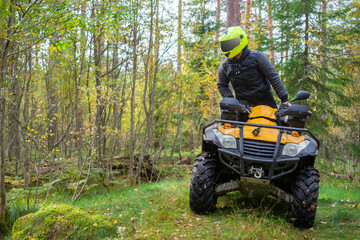 Biker rides a woodland. ATV driver got up to look around. Biker on a yellow ATV. Quad bike driver drive off road. He is into extreme driving. Concept - off-road ATV race. Hobby extreme sport.