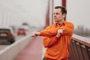 Athlete man stretches his arms on a bridge before training workout