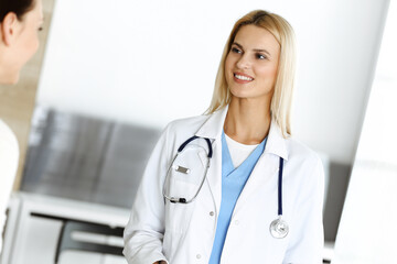 Woman-doctor at work in hospital is happy to communicate with female patient. Blonde physician checks medical history record and exam results. Medicine concept