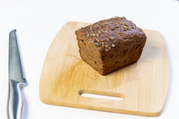 Brown rye bread loaf with sunflower seeds and raisin on cutting board and knife on white background