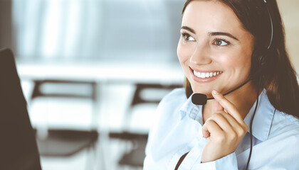 Brunette female customer service representative in a headset is consulting clients online. Call...