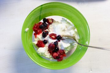Homemade cottage cheese with sour cream and berries in green bowl with spoon on white background