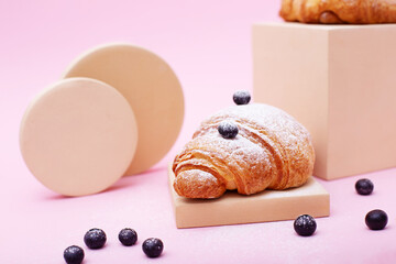 Homemade puff pastry croissant with raw blueberry on modern circle and square podiums on pink background.