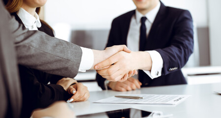 Unknown businessman shaking hands with his colleague or partner above the glass desk in modern office, close-up. Business people group at meeting