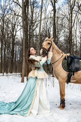 Fototapeta na wymiar beautiful girl in a blue outfit and a light brown horse in a spring forest 