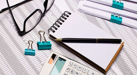 On the desktop are glasses, a notepad with a pen, a calculator, reports, paper clips. Business concept. View from above