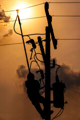 The silhouette of power lineman climbing on an electric pole with a transformer installed. And replacing the damaged hotline clamp, bail clamp, dropout and surge arrester that causes a power failure.