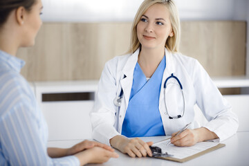 Woman-doctor and patient sitting and talking in hospital or clinic. Blonde therapist is cheerfully...