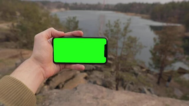 Man hand holding iPhone 11 in Horizontal, Landscape mode. Tourist walking in the forest near lake. Pre-Keyed green screen ready for your content. POV, point of view. Colorado, USA