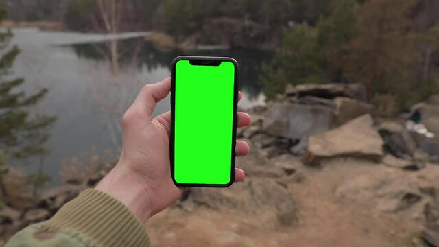 Man hand holding iPhone 11 in vertical or portrait orientation. Tourist walking in the forest near lake. Pre-Keyed green screen ready for your content. POV, point of view. Colorado, USA