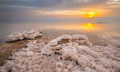 Beautiful Israeli sunrise landscape of the Dead Sea, the lowest place on Earth: salt formations and clouds with sun rising over the Jordanian mountains in the background
