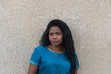 Stock photo of a young African woman looking at the camera. She is standing in front of a wall