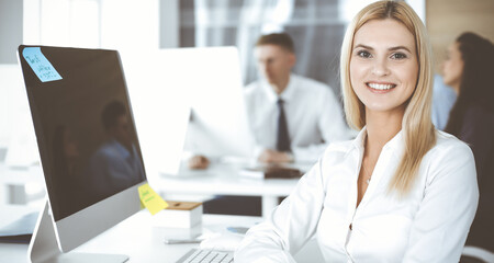 Obraz premium Business woman using computer at workplace in modern office. Secretary or female lawyer smiling and looks happy. Working for pleasure and success