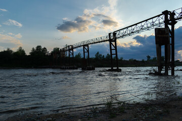 Beautiful waves of the river, on the far background, the old iron structure and a beautiful sunset, the river bank and clouds.