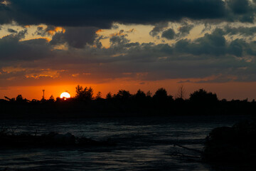 Evening sunset on the background of trees and antennas, in the foreground the river.